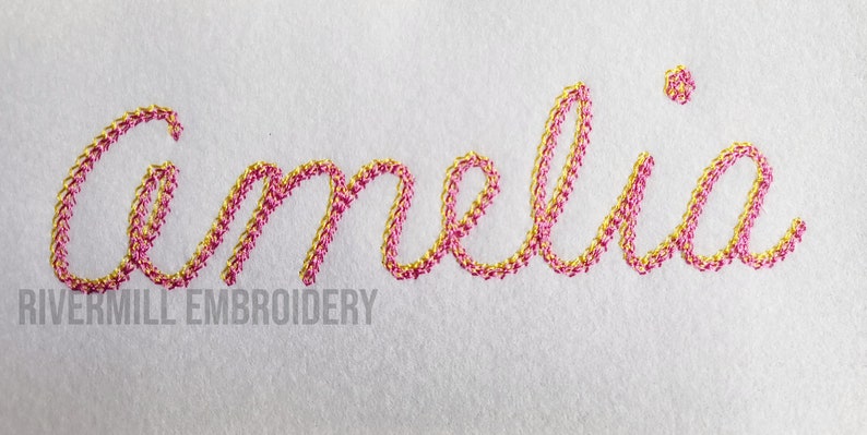Pu&ograve; includere: Nome ricamato "Amelia" in filo rosa e oro su uno sfondo di tessuto bianco. Il testo "Rivermill Embroidery" &egrave; visibile sotto il nome.