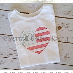 May include: A white t-shirt with a heart-shaped design featuring the American flag. The heart is divided into two sections: one with red and white stripes and the other with blue stars. The text "Rivermill Embroidery" is visible.