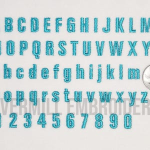 May include: A set of uppercase and lowercase letters and numbers in a teal blue color. The letters are in a block font style. The letters and numbers are embroidered on a white fabric background.