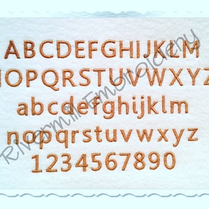 May include: A white background with a brown embroidered alphabet and numbers. The letters are uppercase and lowercase, and the numbers are 1 through 9 and 0.