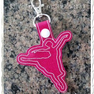 May include: Pink glitter keychain with a white button and a white outline of a ballerina silhouette.