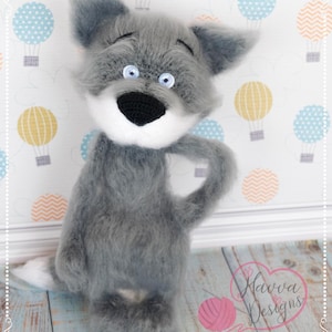 May include: A handmade grey plush wolf toy with a white muzzle and belly, blue eyes, and a black nose. The wolf is standing on a wooden surface with a backdrop of hot air balloons. The toy has a fluffy texture and is posed with one arm raised.
