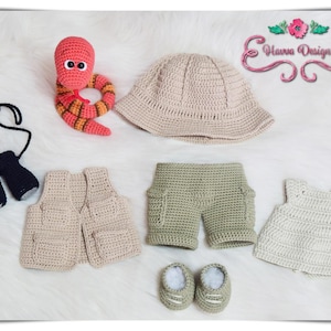 May include: A collection of handmade crochet baby clothes and accessories. Includes a red and orange worm, a beige bucket hat, a beige vest, green shorts, a white dress, black mittens, and beige shoes. The items are arranged on a white, fluffy surface.