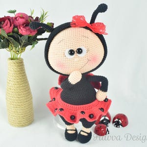 May include: A handmade crochet ladybug doll with a black body, red skirt, and a red bow. The doll has large, expressive eyes and is standing near a vase of pink flowers. The ladybug doll is a whimsical, handcrafted item.