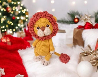 May include: A handmade crochet lion toy with a yellow body and a reddish-brown mane and tail. The lion is sitting on a white surface, with a Christmas tree and wrapped gifts in the background. The toy is approximately 6 inches tall.