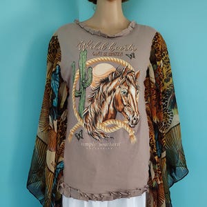 May include: A beige short-sleeved top with ruffled trim at the neckline and hem. The front features a graphic of a horse, a cactus, and a rope with the text Wild hearts CAN'T BE BROKEN and simply southern. The sleeves are long, sheer, and patterned.