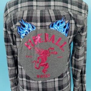 May include: Gray plaid flannel shirt with a gray patch on the back. The patch has a red devil with flames and the text "Fireball Whiskey" in red.