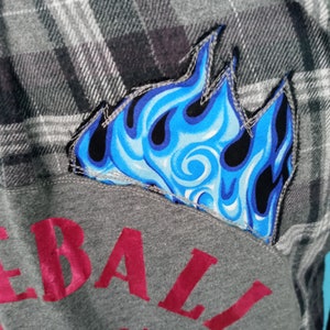 May include: A gray flannel shirt with a blue flame patch and a red "Rebel" logo on the front.