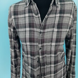 May include: A long-sleeved plaid shirt with a button-up front. The shirt is gray with black and white plaid.