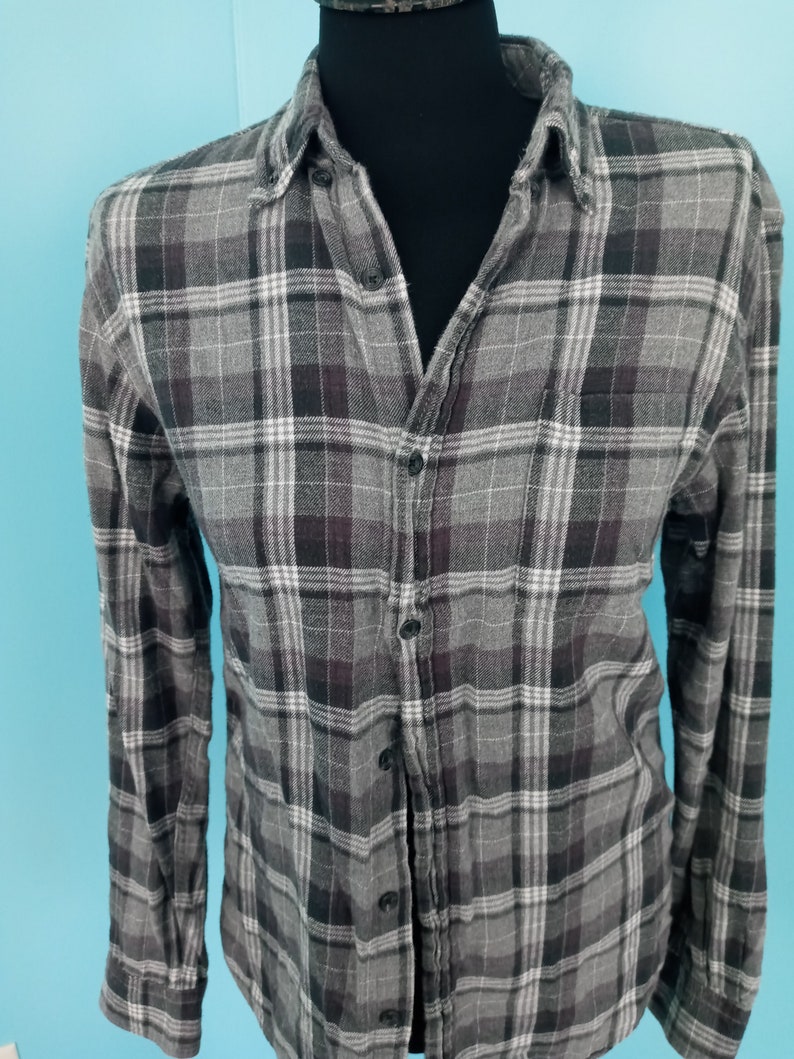 May include: A long-sleeved plaid shirt with a button-up front. The shirt is gray with black and white plaid.