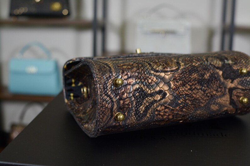 May include: Close-up of a brown and gold snakeskin-patterned handbag. The bag has gold-coloured hardware and a textured surface. The bag is a stylish accessory.