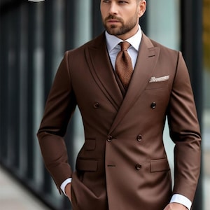 May include: A brown double-breasted suit with a matching vest, white dress shirt, and patterned tie. The suit has a pocket square and is worn by a person. The image includes the text "BESPOKE TAILORING".