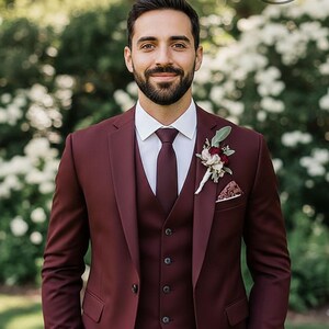 May include: A three-piece burgundy suit with a white dress shirt and matching burgundy tie. A floral boutonniere and pocket square add detail. The suit is tailored with a classic fit, perfect for formal events.