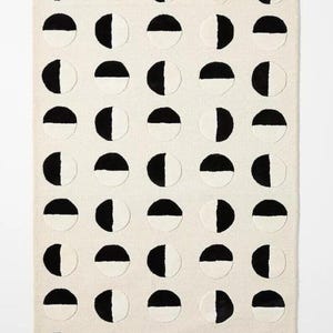 May include: A rectangular rug with a repeating pattern of black and white half-circles. The rug has a cream-colored background and the half-circles are arranged in a grid-like fashion. The rug is a modern home decor item.