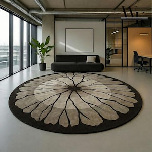Può includere: Un grande tappeto rotondo con un design floreale in un ambiente ufficio moderno. Il tappeto presenta un bordo marrone scuro, con un motivo floreale marrone chiaro e grigio al centro. Il tappeto è posto davanti a un divano nero.