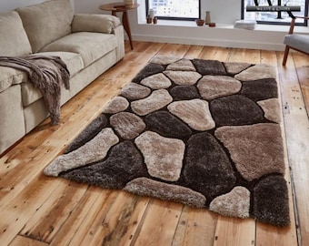 May include: A rectangular rug featuring a stone-effect design in brown, beige, and black. The rug is laid on a wooden floor, with a beige sofa in the background. The pattern mimics large, irregularly shaped stones, creating a natural aesthetic.