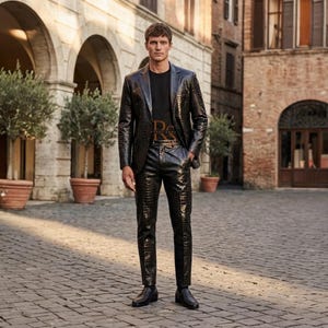 May include: A black suit with a textured crocodile skin pattern, consisting of a single-breasted blazer and matching trousers. The suit is worn over a black t-shirt featuring the gold letters RS on the chest, paired with black leather loafers.