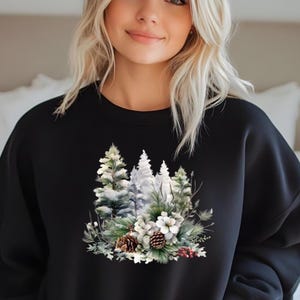 May include: Black sweatshirt featuring a winter forest design. The graphic includes snow-covered pine trees, white flowers, pine cones, and red berries. The design is centered on the front of the crew neck sweatshirt.