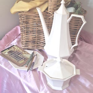 May include: A white ceramic coffee pot and a matching lidded sugar bowl with an angular, faceted design. The set is accompanied by a small white plate holding two pens and a rectangular card featuring the text: If you love someone, showing them is better than telling them. If you stop loving someone, telling them is better than showing them.