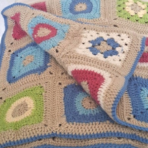 May include: A handmade crochet blanket featuring a repeating granny square pattern. The squares are constructed with a neutral beige yarn base, accented by vibrant pops of blue, light blue, lime green, and magenta yarn throughout the design.