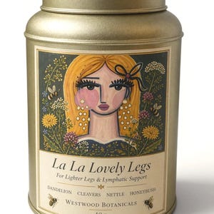 May include: A gold-colored metal tin with a lid, featuring a label with the text "La La Lovely Legs." The label includes an illustration of a woman with blonde hair and floral elements. The tin contains 40 grams of product.