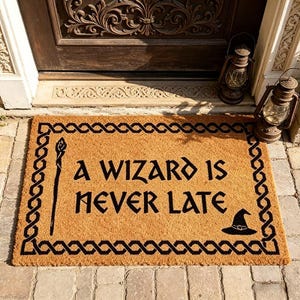 Pode incluir: Um capacho retangular feito de fibras naturais com o texto "A WIZARD IS NEVER LATE" em preto. O tapete apresenta uma borda preta com um design de varinha e chapéu de bruxo.