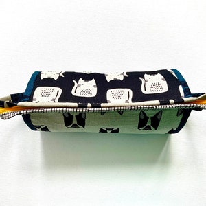 May include: A black and white fabric pencil case with a cat print design. The case has a yellow zipper and a blue and white fabric lining.