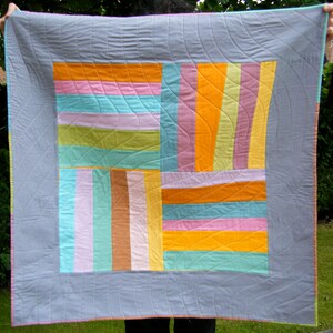 May include: A gray quilt with a patchwork design featuring various shades of pink, orange, green, and blue. The quilt is quilted with a wavy pattern.