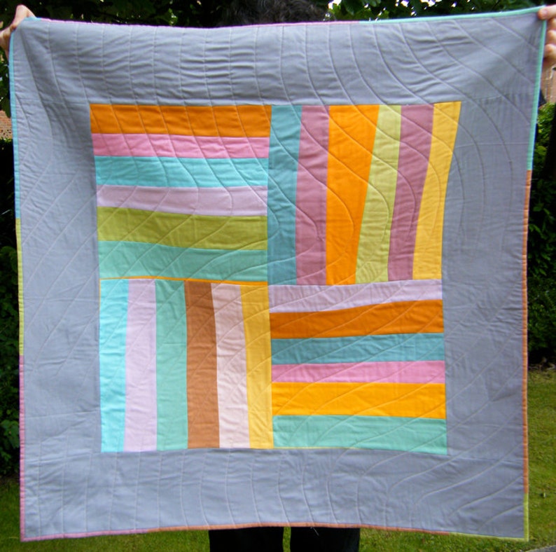 May include: A gray quilt with a patchwork design featuring various shades of pink, orange, green, and blue. The quilt is quilted with a wavy pattern.