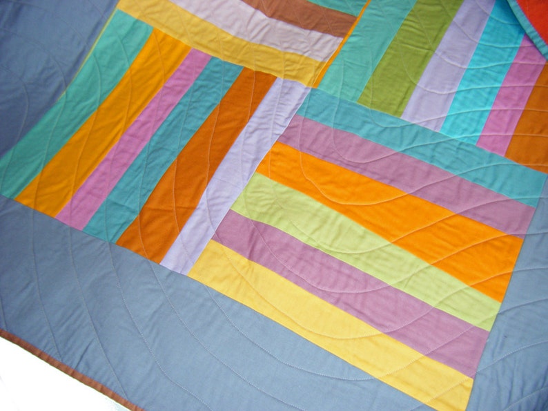 May include: A colorful quilt with a patchwork design featuring stripes and curves in shades of blue, green, yellow, orange, pink, and purple.