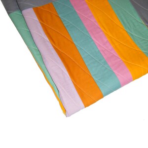 May include: A colorful striped quilt with orange, pink, green, and gray fabric. The quilt is folded in half and the fabric is quilted with a diamond pattern.