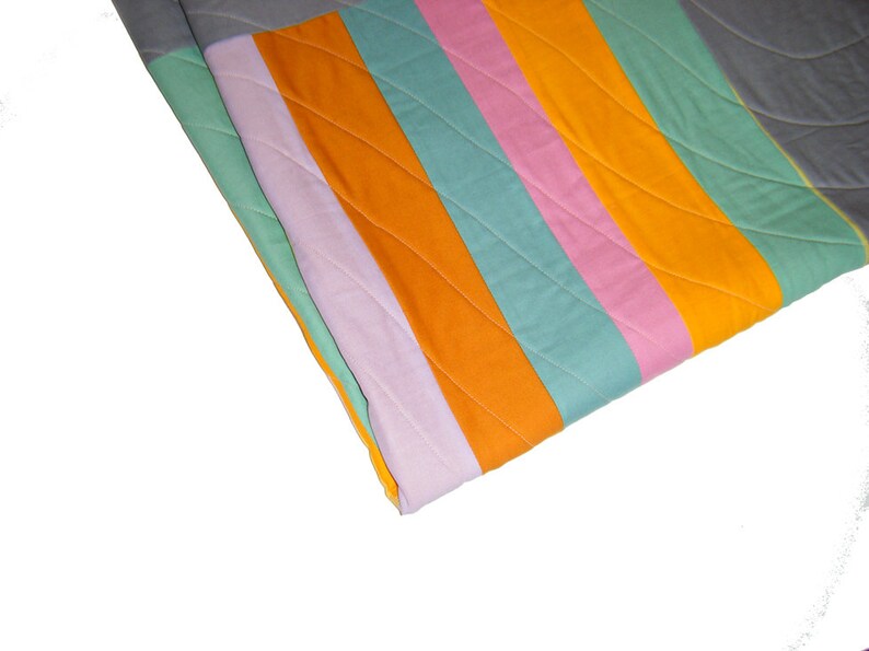 May include: A colorful striped quilt with orange, pink, green, and gray fabric. The quilt is folded in half and the fabric is quilted with a diamond pattern.
