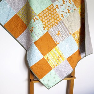 May include: A patchwork baby quilt featuring a variety of fabrics in shades of orange, yellow, green, and grey. The quilt has a repeating pattern of foxes and trees.