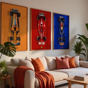 May include: Three framed Formula 1 car prints. The prints feature overhead views of race cars against orange, red, and blue backgrounds. The room includes a white sectional sofa with orange pillows and a wooden coffee table.