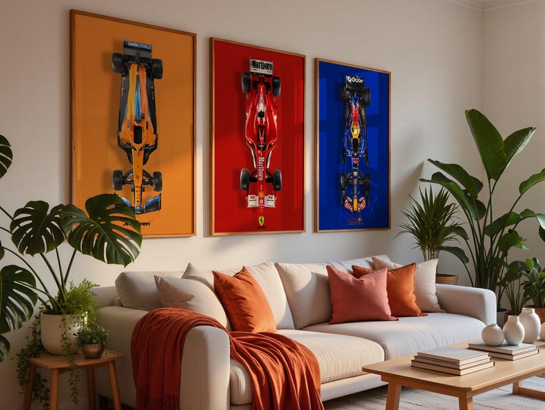May include: Three framed Formula 1 car prints. The prints feature overhead views of race cars against orange, red, and blue backgrounds. The room includes a white sectional sofa with orange pillows and a wooden coffee table.