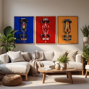 May include: Three framed Formula 1 car art prints. The prints feature top-down views of race cars against blue, red, and orange backgrounds. The room includes a beige sectional sofa, a wooden coffee table, and potted plants.