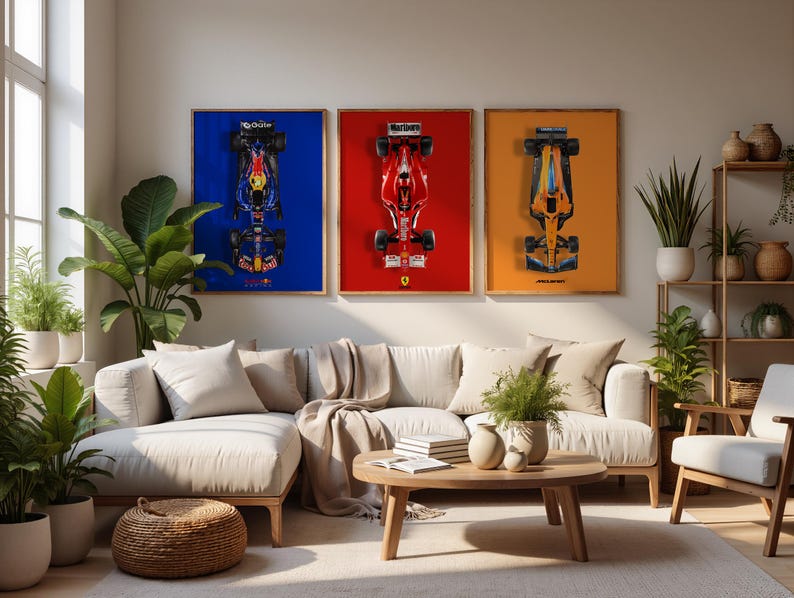 May include: Three framed Formula 1 car art prints. The prints feature top-down views of race cars against blue, red, and orange backgrounds. The room includes a beige sectional sofa, a wooden coffee table, and potted plants.