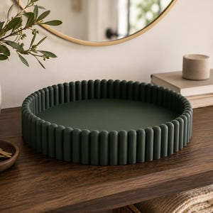 May include: A circular dark forest green tray featuring a raised, ribbed, or fluted edge design. The tray has a smooth, flat interior base and a consistent matte finish throughout its entire structure, providing a clean and uniform appearance.