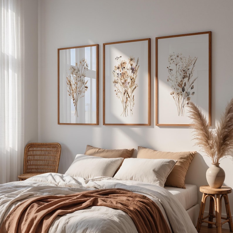 May include: Three framed botanical prints with dried flowers in shades of beige, brown, and tan hang above a bed with neutral-colored bedding. The frames are a warm brown, and the overall aesthetic is natural and calming.