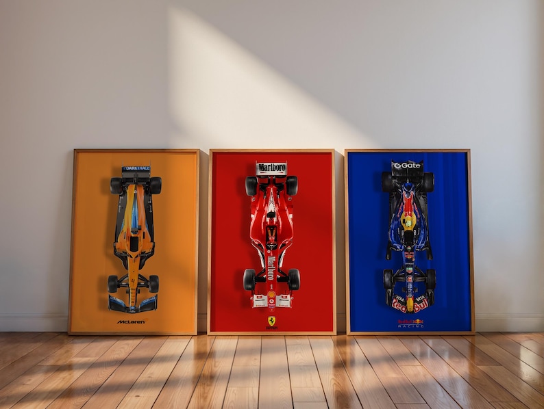 May include: Three framed Formula 1 race car prints. The first print features an orange and blue car on an orange background. The second print has a red car on a red background. The third print shows a blue and black car on a blue background.