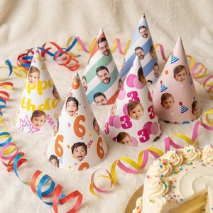 May include: A selection of personalised birthday party hats featuring printed faces. The hats are decorated with numbers and the words "Happy Birthday". The image also includes colourful streamers and a cake with sprinkles.