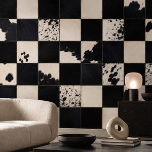 May include: A wall covering featuring a checkerboard pattern of alternating solid black and white cowhide squares. The squares are stitched together with visible seams, creating a grid of contrasting textures and natural animal hide patterns.