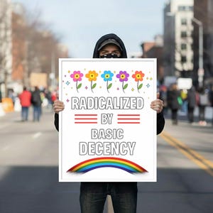 Pode incluir: Uma pessoa segurando uma placa branca com o texto "RADICALIZED BY BASIC DECENCY". A placa apresenta ilustrações de flores coloridas e um arco-íris. A pessoa está vestindo um moletom preto com capuz e jeans.
