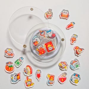May include: A selection of clear acrylic charms with vibrant cartoon animal illustrations, such as rabbits, bears, and fish. The charms feature red and gold details, with some displaying Chinese characters. A clear, circular object with a string is in the center.
