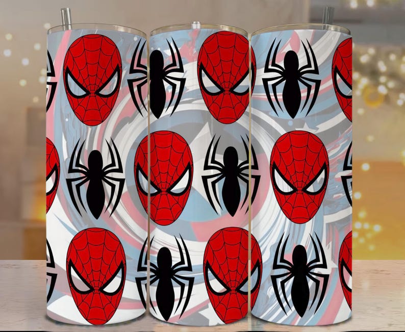 Op de afbeelding: Drie roestvrijstalen bekers met een herhaald patroon van Spider-Mans masker en spinnenembleem. Het ontwerp bevat rode, witte en blauwe wervelingen. Elke beker heeft een zilveren rietje.
