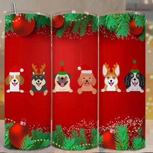 May include: A set of three red Christmas-themed tumblers featuring cartoon dogs wearing Santa hats and reindeer antlers. Each tumbler has a red background with Christmas ornaments and green pine branches. The tumblers are approximately 8 inches tall.