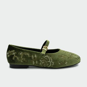Pu&ograve; includere: Ballerine Mary Jane in velluto verde oliva con ricami floreali. Le scarpe hanno un cinturino con fibbia color oro. Le ballerine hanno la punta arrotondata e un tacco basso.