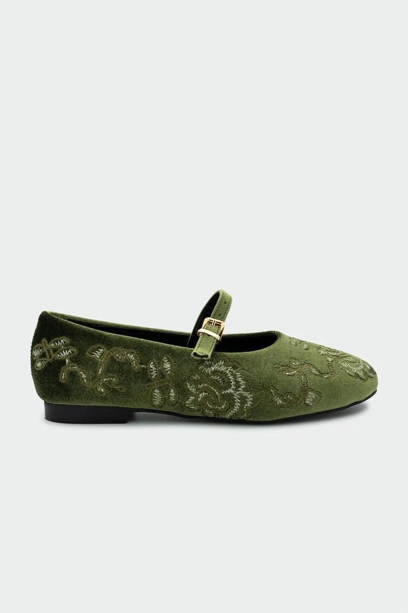 Pu&ograve; includere: Ballerine Mary Jane in velluto verde oliva con ricami floreali. Le scarpe hanno un cinturino con fibbia color oro. Le ballerine hanno la punta arrotondata e un tacco basso.