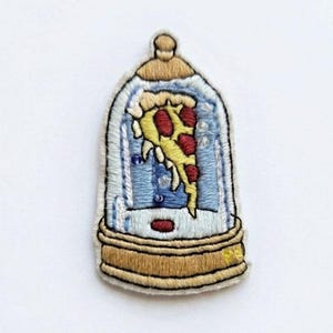 Puede incluir: Parche bordado con una porción de pizza dentro de una cúpula de cristal. El parche tiene una base dorada, un interior azul y una porción de pizza amarilla y roja. Fondo blanco.