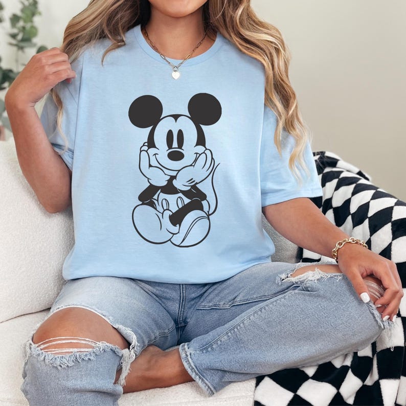 Peut inclure: T-shirt bleu clair avec une illustration en noir et blanc de Mickey Mouse. Le personnage de dessin anim&eacute; est repr&eacute;sent&eacute; avec ses mains sous son menton. Le t-shirt est en mati&egrave;re douce et a des manches courtes.